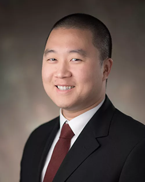 Portrait of a doctor in a suit smiling against a mottled background.