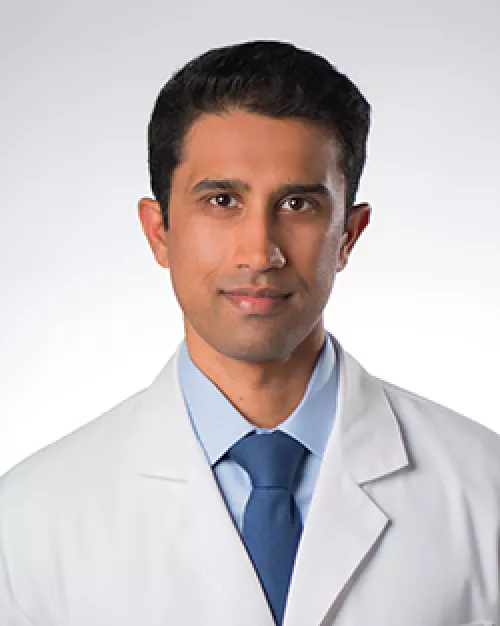 Portrait of a doctor in a white coat smiling against a white background.