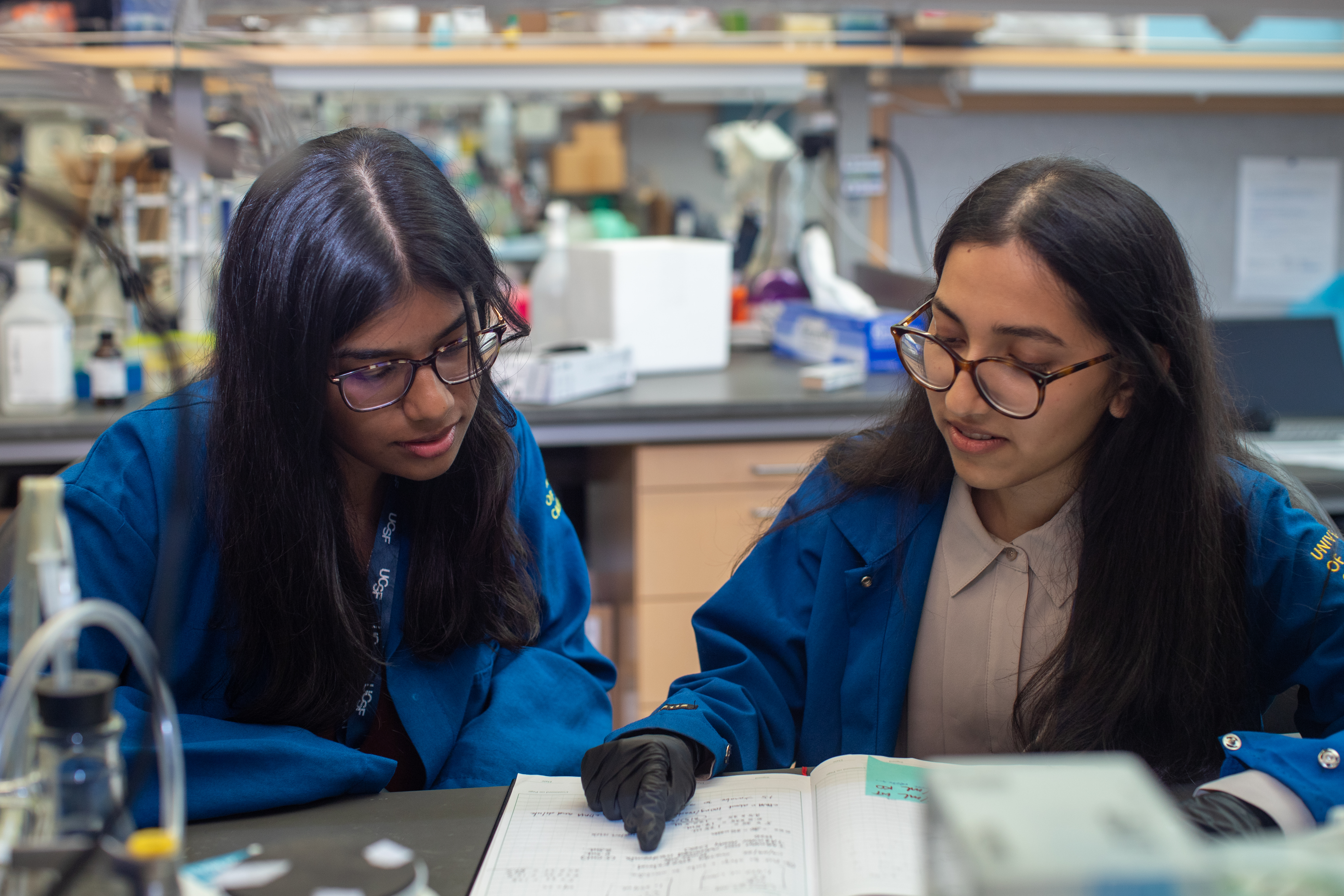 Two people sitting at a lab bench looking at a lab notebook