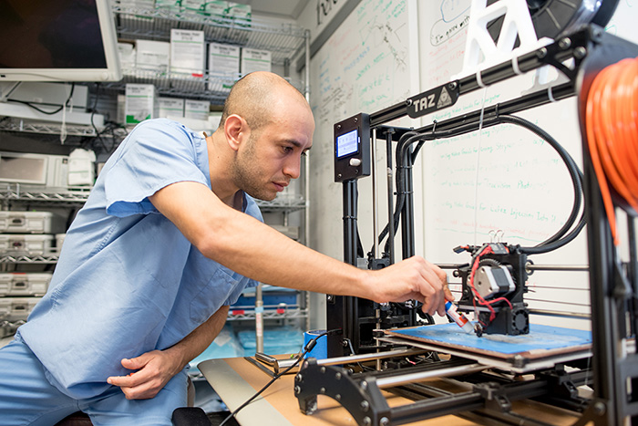 Photo of Dr. Rodriguez Rubio leans over a 3D printer.